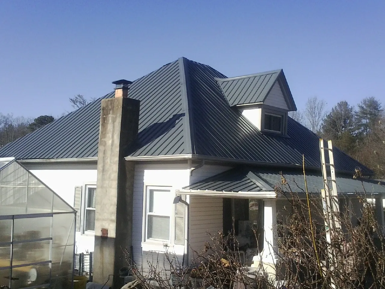 Dark blue standing seam metal roof on a white farmhouse with dormer — Slate & Tile Roof Repair by Roofing Brothers in Tigerton