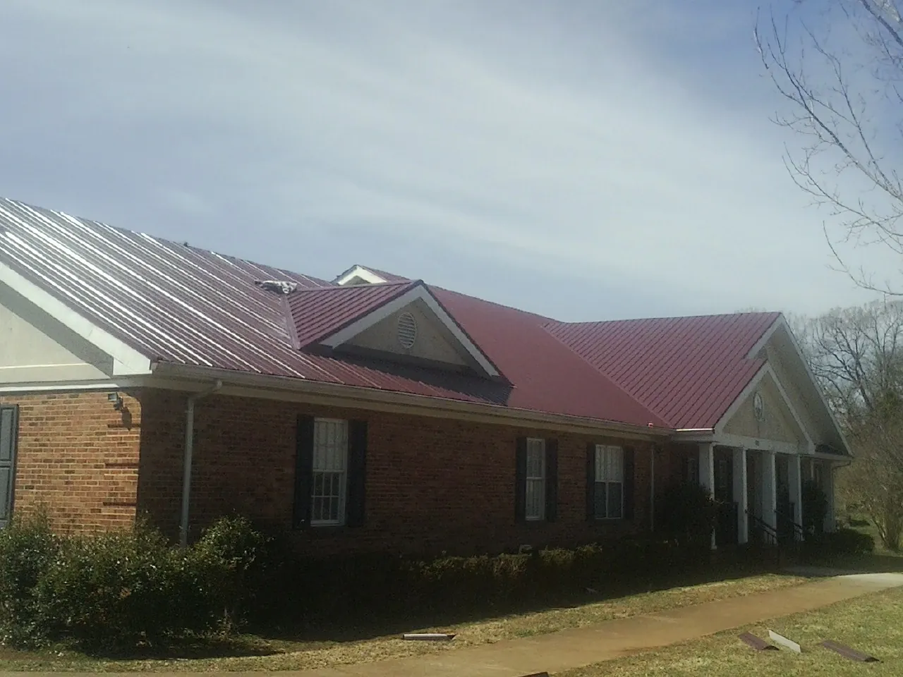 Red metal roof with gabled entries on a long brick building, from a Hail Damage Roof Repair job in Tigerton
