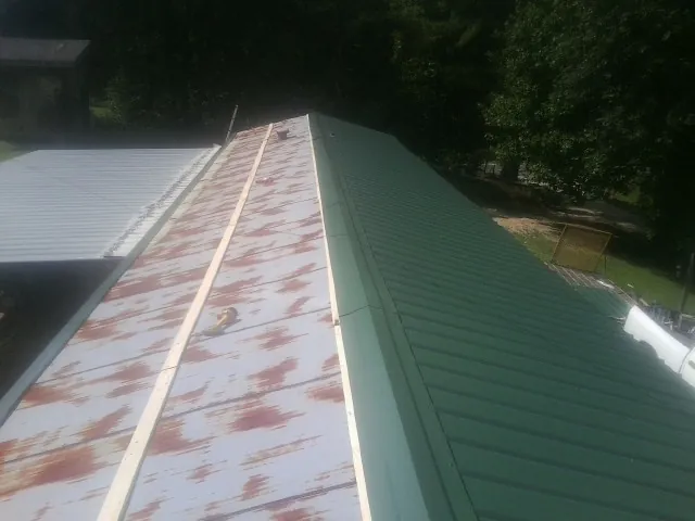 Old rusted panels beside newly installed green metal roofing — Wind Damage Roof Repair by Roofing Brothers in Tigerton