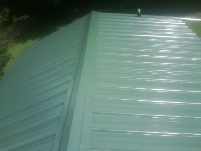 New green metal panels meeting at the ridge of a roof — Flat Roof Repair work by our crew in Tigerton
