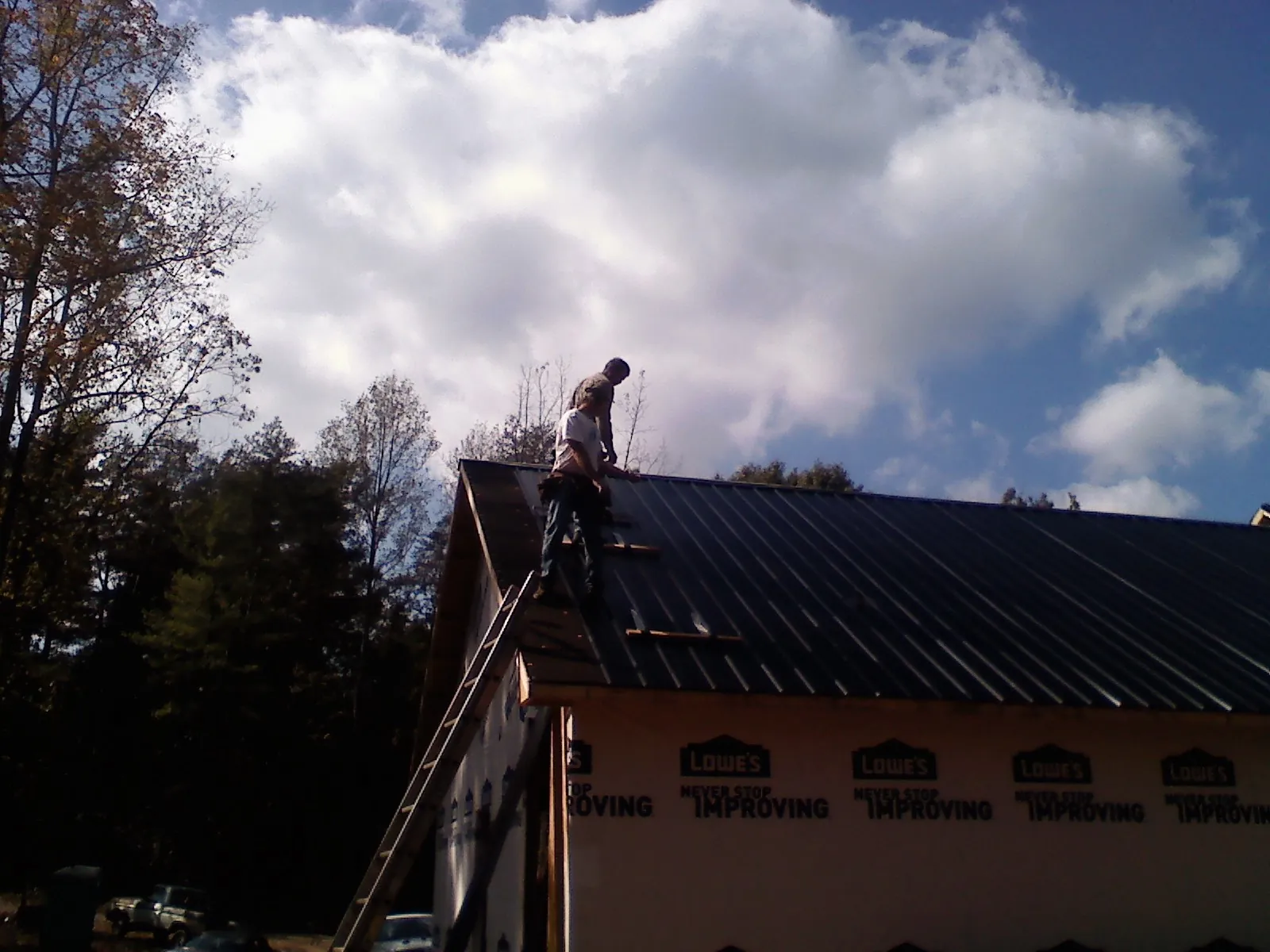 Roofer fastening dark metal panels high against a cloudy sky, from a Roof Inspection job in Tigerton
