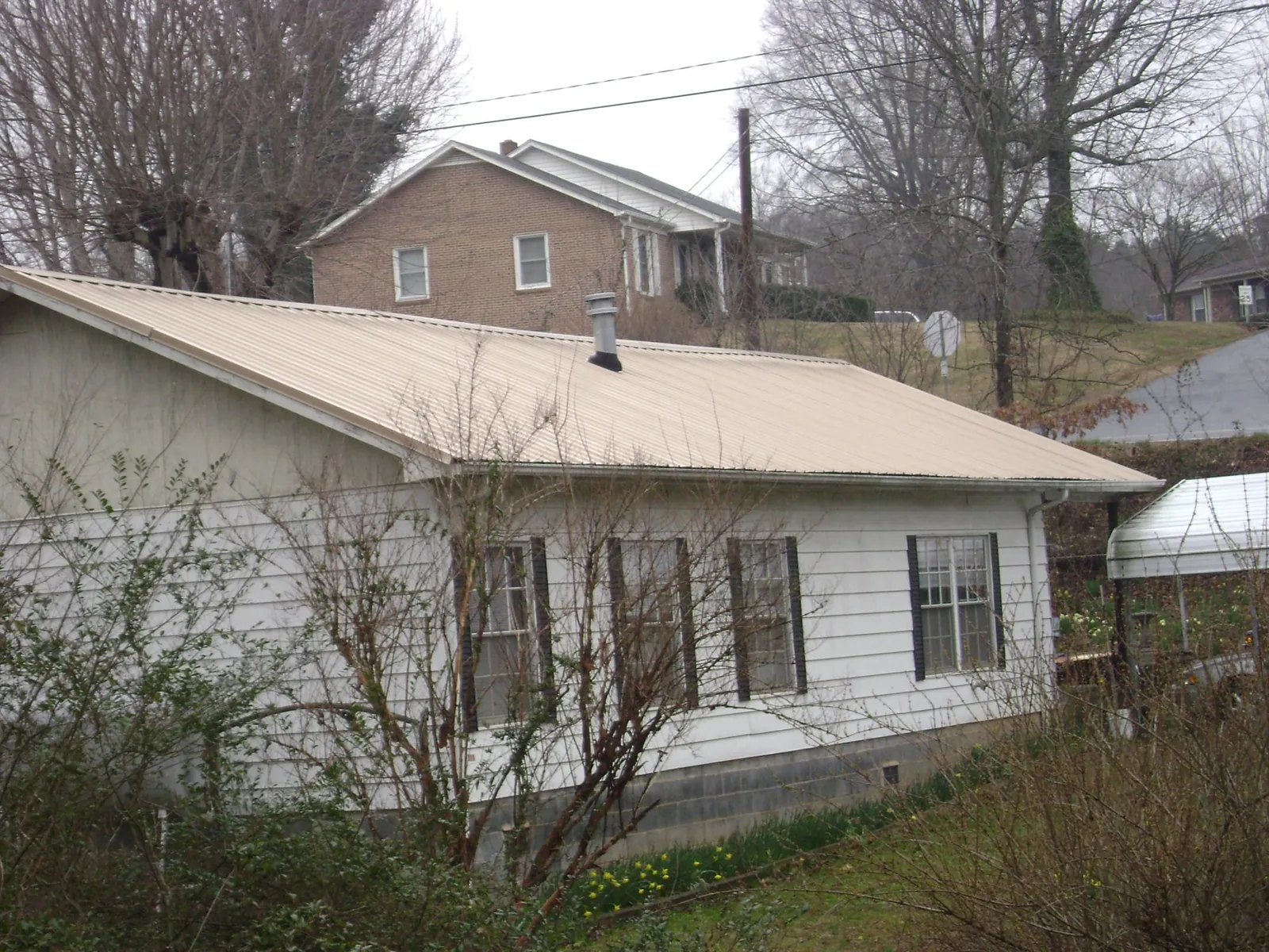 Tan metal roof on a white sided house set into a hillside — Commercial Roofing by Roofing Brothers in Tigerton